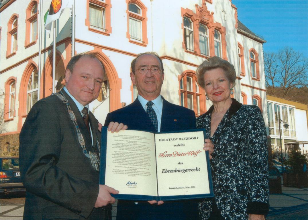 Diter Wolf (Mitte), in Begleitung seiner Ehefrau (rechts), erhält von Bürgermeister Michael Lieber (links) die Urkunde zum Ehrenbürger der Stadt Betzdorf.